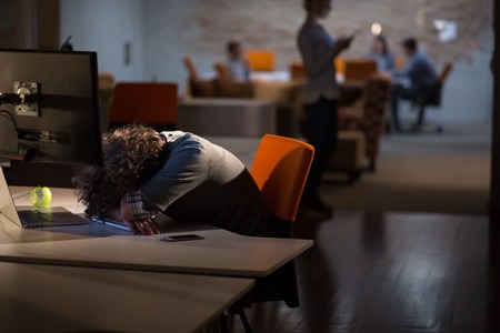 A time for relax. Young tired casual businessman relaxing at the desk in his night officeの写真素材
