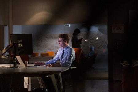Young man working on computer at night in dark office. The designer works in the later time.の写真素材