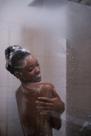 Woman in the shower,beautiful black young female showering under refreshing water, healthy lifestyle, enjoying time in luxury spa resortの写真素材