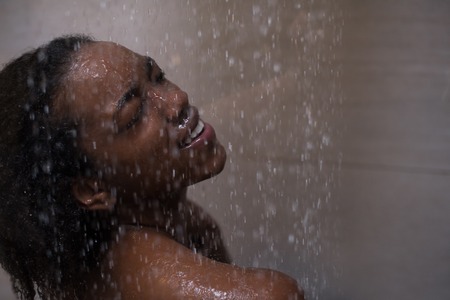 Woman in the shower,beautiful black young female showering under refreshing water, healthy lifestyle, enjoying time in luxury spa resortの写真素材