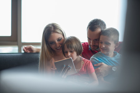 Happy Young Family Playing Together with tablet at home sitting on the sofa