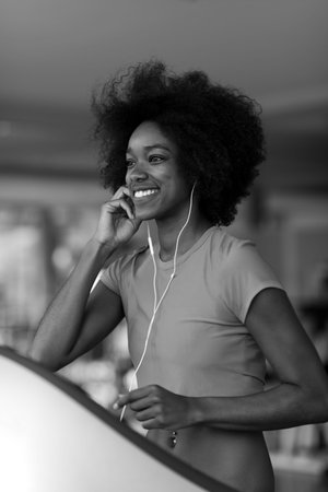 afro american woman running on a treadmill at the gym while listening music on earphones