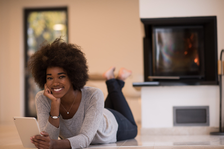 beautiful young black women using tablet computer on the floor of her luxury home in front of fireplace at autumn dayの写真素材