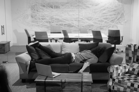 A young casual businessman sleeping on a sofa during a work break in a creative officeの写真素材