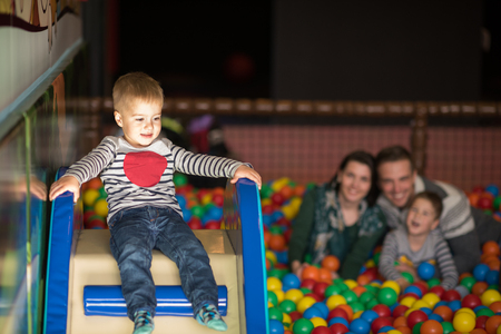 Happy young parents are playing with their kids at pool with colorful balls in a children's playroomの写真素材