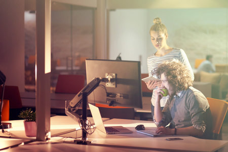 Two young designers are working on a new project in the night office using modern technology