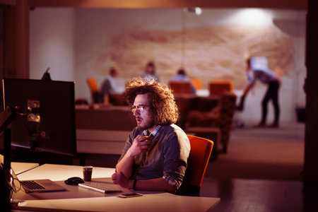 Young man working on computer at night in dark office. The designer works in the later time.