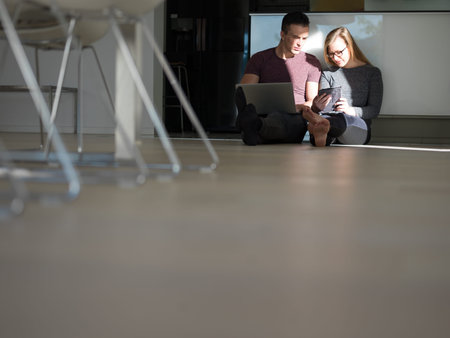 Young couple relaxing at luxurious home with tablet and laptop computers reading on the floor
