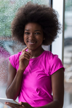beautiful african american woman using tablet computer from home while rain and bad weather is...