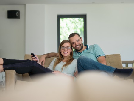 Young couple on the sofa watching television together in their luxury homeの写真素材