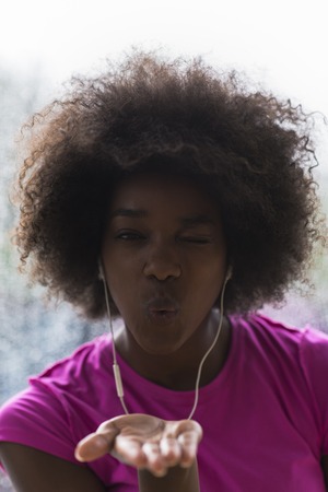 portrait of young afro american woman in gym on workout break while listening music on earphone  and dancing  rainy day and bad weather outdooorの写真素材