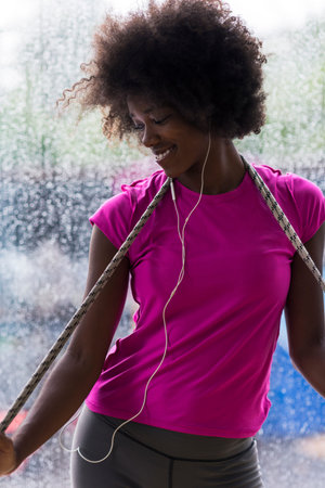 portrait of young afro american woman in gym on workout break while listening music on earphone  and dancing  rainy day and bad weather outdooorの写真素材