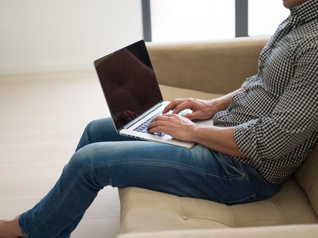 Young, handsome man using laptop sitting on sofaの写真素材