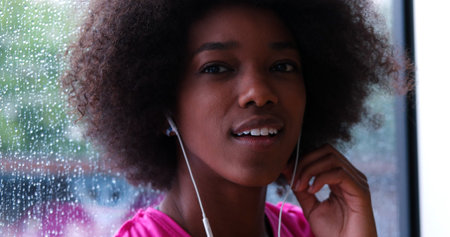 portrait of young afro american woman in gym on workout break while listening music on earphone and dancing rainy day and bad weather outdooorの写真素材