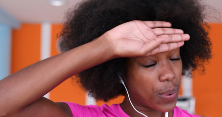portrait of young afro american woman in gym on workout break while listening music on earphoneの写真素材