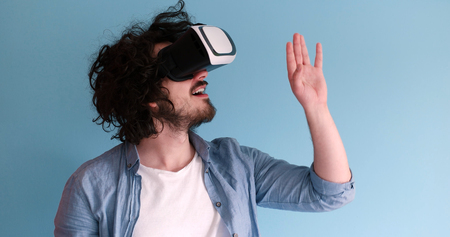 Happy man getting experience using VR headset glasses of virtual reality, isolated on blue backgroundの写真素材