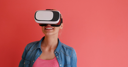 Happy girl getting experience using VR headset glasses of virtual reality, isolated on red backgroundの写真素材