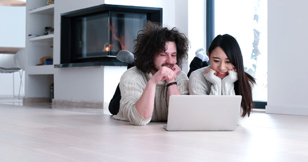 Young beautiful multiethnic couple using a laptop and doing shopping online at home on the floorの写真素材