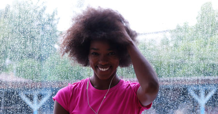 portrait of young afro american woman in gym on workout break while listening music on earphone and dancing rainy day and bad weather outdooorの写真素材