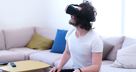 happy man getting experience using VR-headset glasses of virtual reality at homeの写真素材