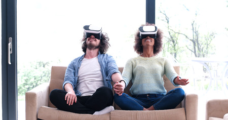Multiethnic Couple using virtual reality headset in living room at home  people playing game with new trends technologyの写真素材