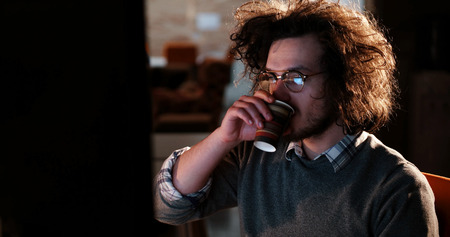 Tired businessman working late doing overtime in office at night drinking coffee to go on.の写真素材