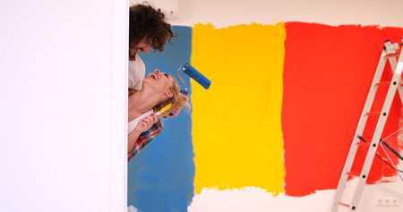 portrait of happy smiling young couple painting interior wall of new house  peeking from behind the wallの写真素材