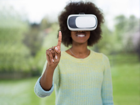 Happy african american girl getting experience using VR headset glasses of virtual reality at homeの写真素材