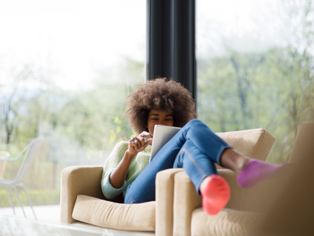 Young african american woman at home relaxing in her luxury lliving room reading a digital tablet  surf internet and workの写真素材