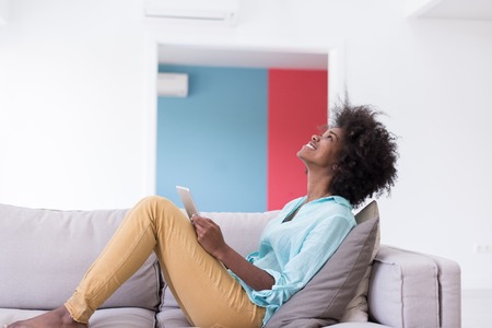 Young african american woman at home relaxing in her luxury lliving room reading a digital tablet PC surf internet and workの写真素材