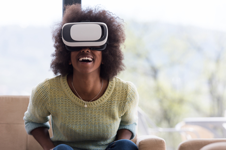 Happy african american girl getting experience using VR headset glasses of virtual reality at homeの写真素材