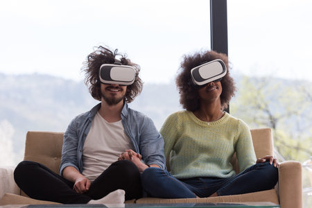 Multiethnic Couple using virtual reality headset in living room at home  people playing game with new trends technologyの写真素材