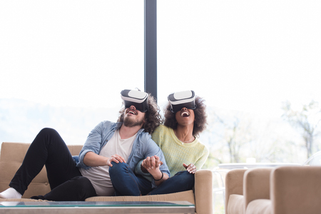 Multiethnic Couple using virtual reality headset in living room at home  people playing game with new trends technologyの写真素材