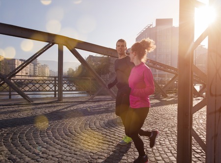 healthy young couple jogging in the city at early morning with sunrise in backgroundの写真素材