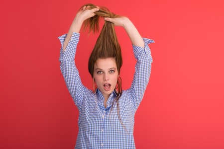 Portrait of a beautiful positive young woman while playing with her long silky hair isolated on red backgroundの写真素材