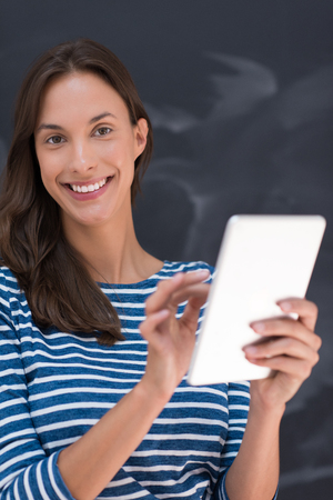 Happy young woman using tablet computer in front of chalk drawing boardの写真素材