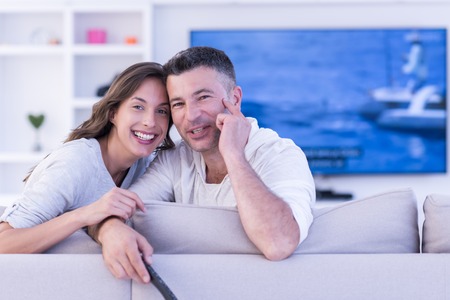 Young couple on the sofa watching television together in their luxury homeの写真素材