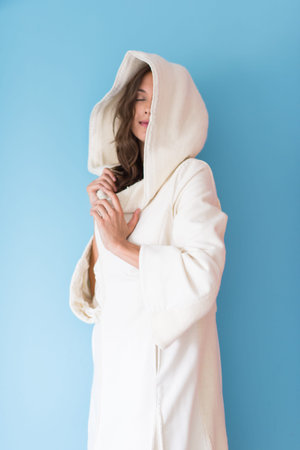 portrait of Beautiful young woman wearing a white coat with hood isolated on blue backgroundの写真素材