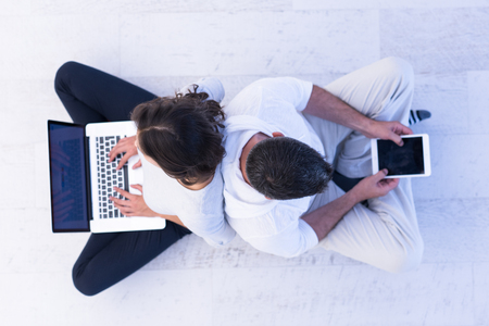 top view of a young couple relaxing at home with tablet and laptop computers reading on the floorの写真素材