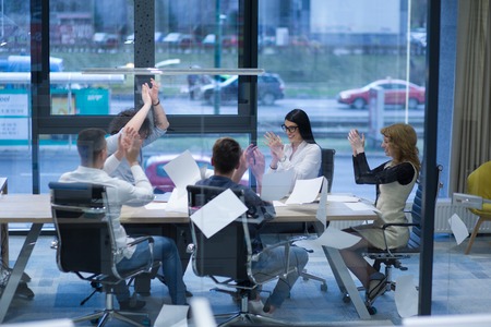 Group of young business people throwing documents and looking happy while celebrating success at their working places in startup officeの写真素材