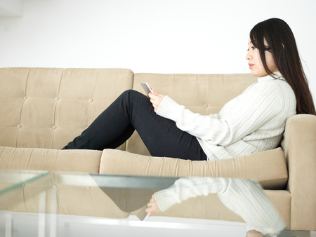 young happy asian woman sitting on sofa using Digital Tabletの写真素材