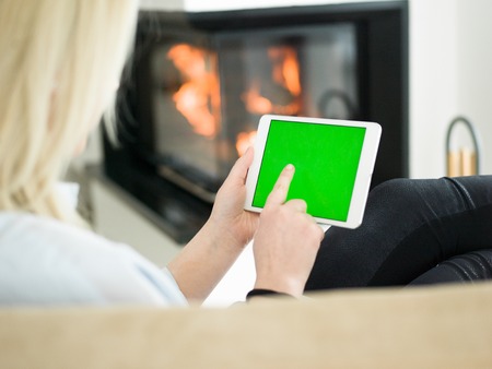 beautiful young woman surfing web using tablet computer in front of fireplace on cold winter day at homeの写真素材