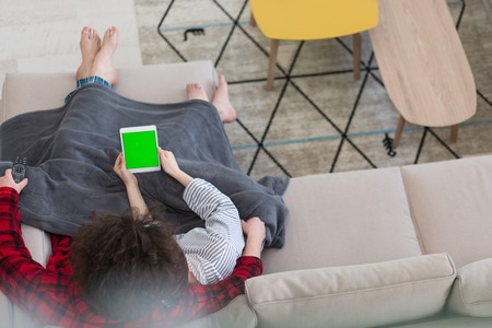 Young couple relaxing at  home using tablet computers reading in the living room on the sofa couch.の写真素材