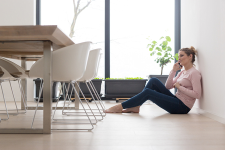 young happy woman sitting on the floor and using mobile phone at homeの写真素材