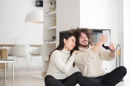 beautiful young multiethnic couple using tablet computer in front of fireplace on cold winter day at homeの写真素材