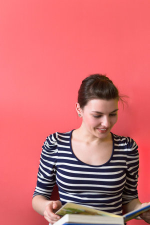 Young casual woman sitting on floor and reading a book, isolated on red background