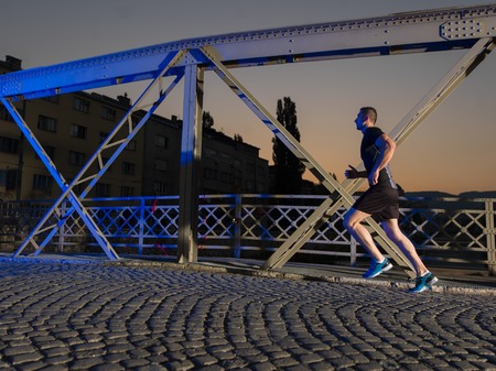 urban sports, young healthy man jogging across the bridge in the city at early morning in nightの写真素材