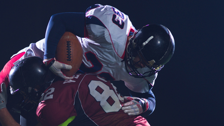 American football players in action at night game time on the fieldの写真素材