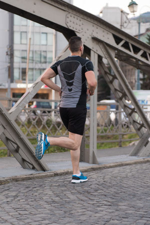young sporty man jogging across the bridge at sunny morning in the cityの写真素材