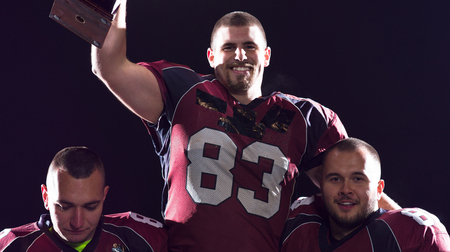 happy american football team with trophy celebrating victory on night fieldの写真素材